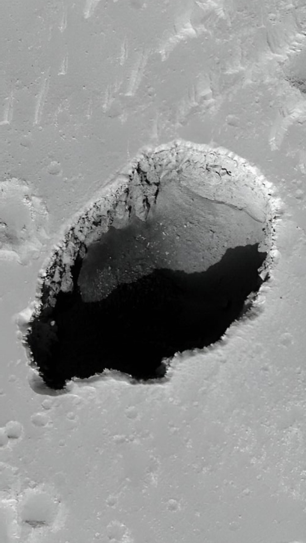 Black and white image of the surface of mars with a deep dark hole