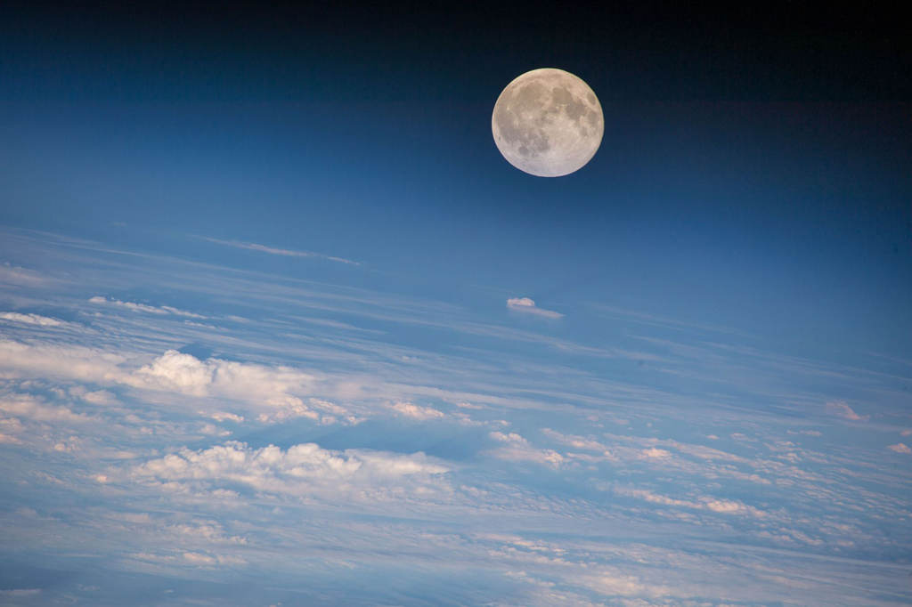 image of the moon above the white clouds and blue surface of Earth