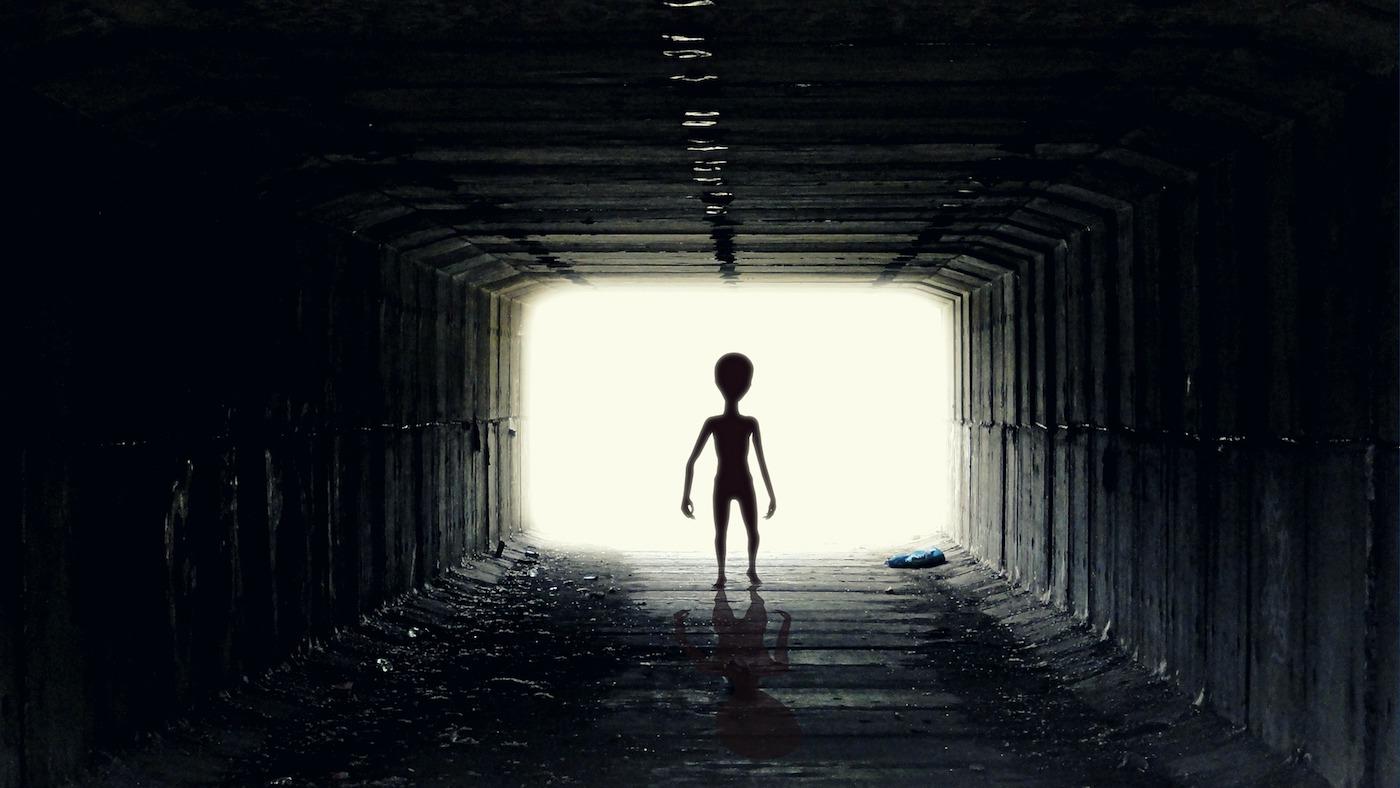 small alien-figure against a light background walking towards tunnel