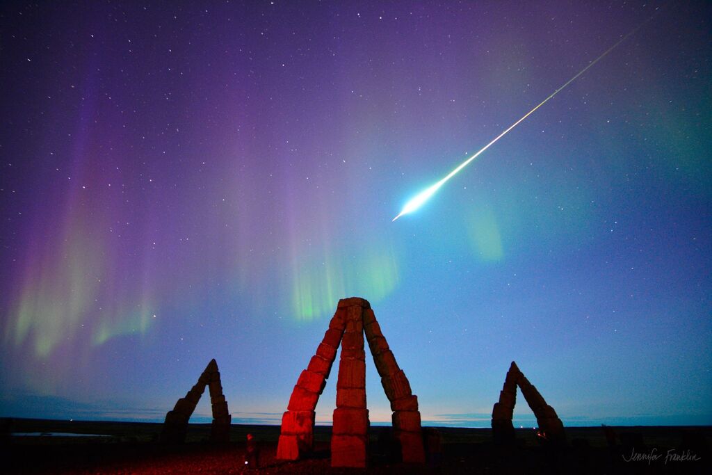 formations with a blue, purple, and green sky as a bright object passes across