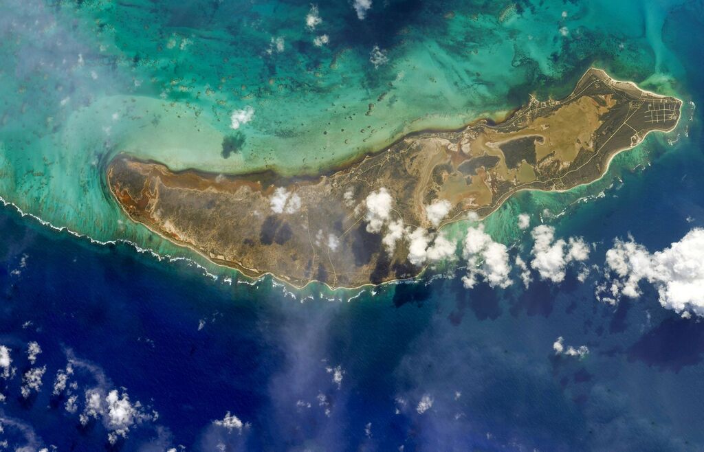 view of the island from the ISS: land "sandwiched" between the blue ocean and white clouds.