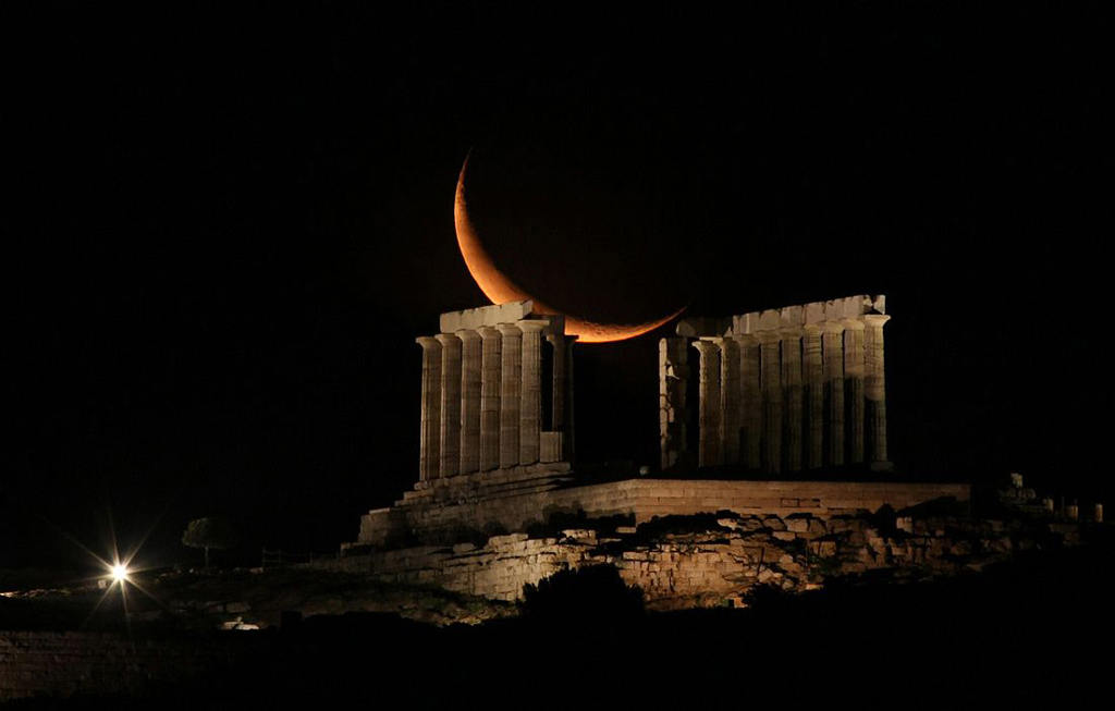 giant image of the orange moon behind the pillars of an ancient temple