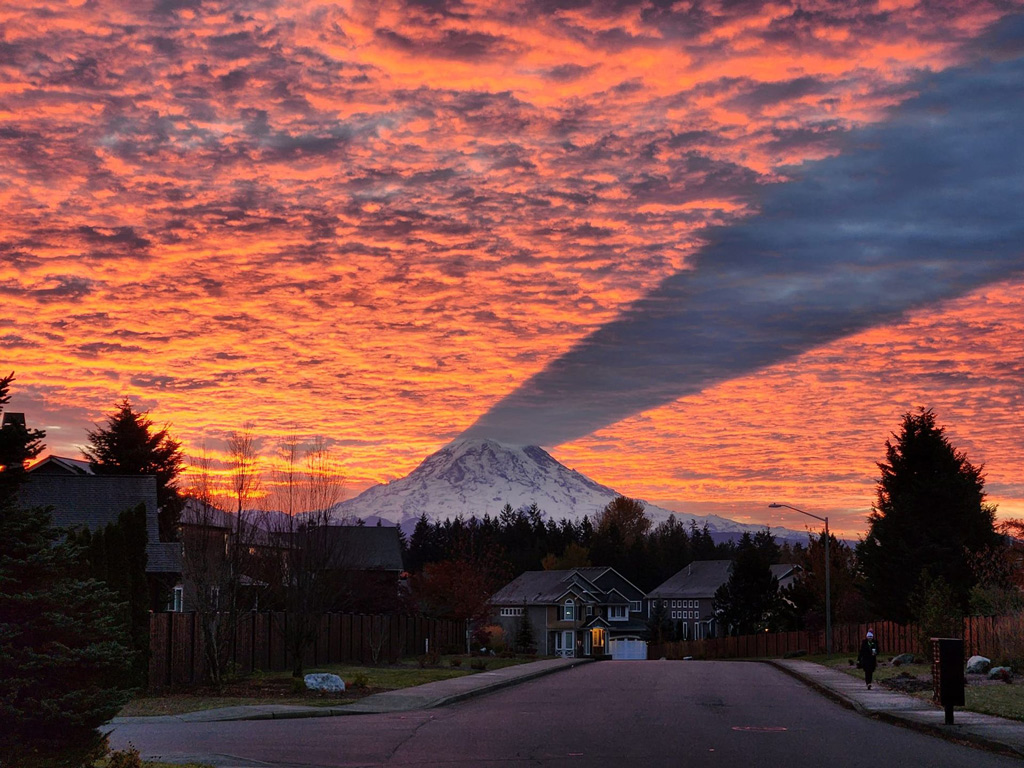 Mount Rainier volcano casts a long shadow on the underside of a sunrise cloud deck over a quiet neighborhood in Washington state.