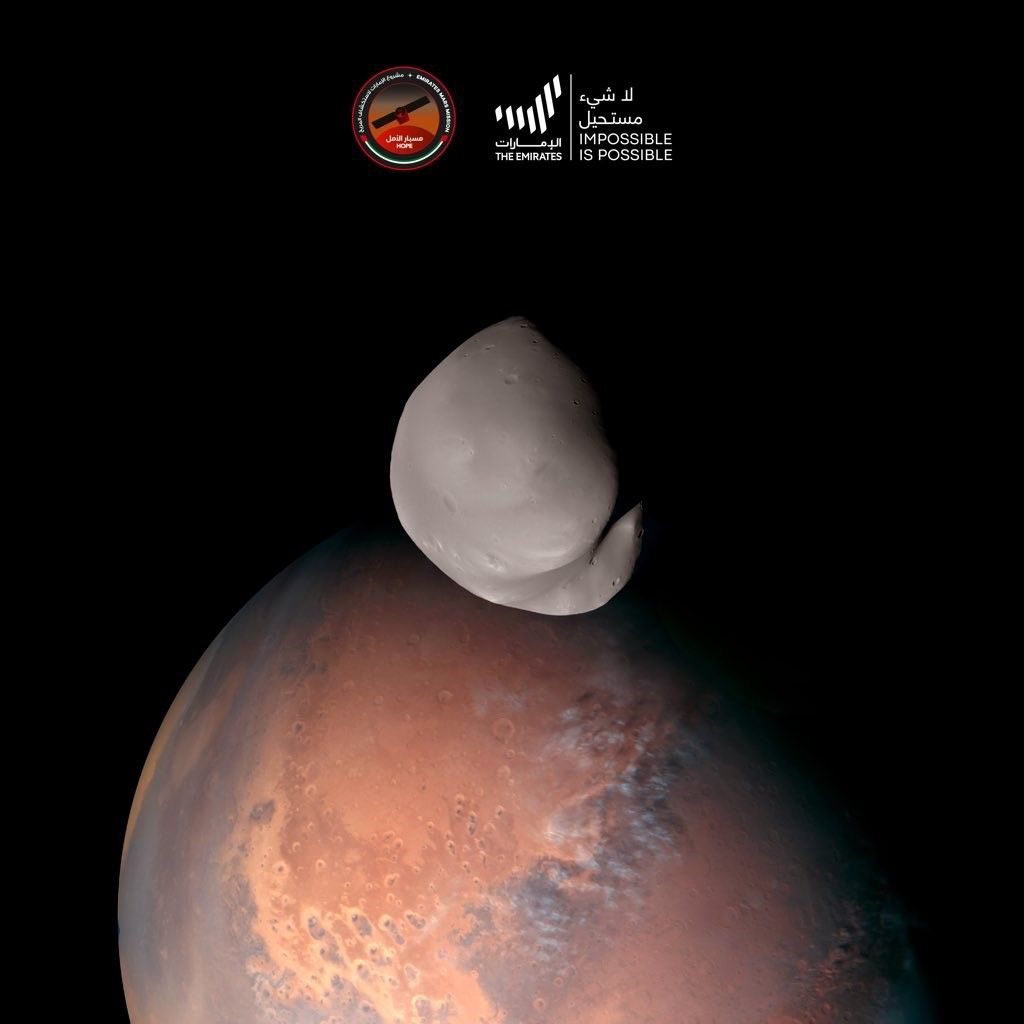 close-up image of the smooth gray moon with the red planet in the background.