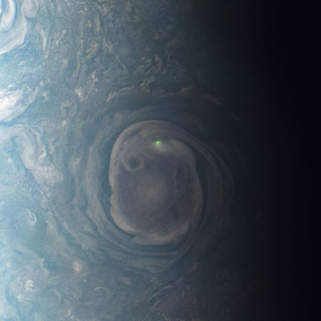 Close up of Jupiter with a small bright green light emitting from a storm