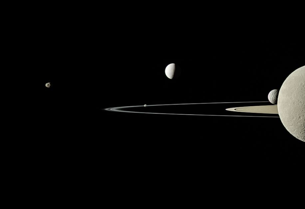 Image of Saturn on the corner right with the moons orbiting against the black background of outer space