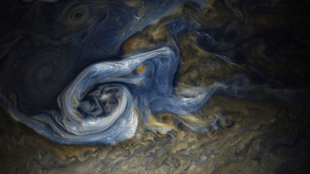 a close up view of Jupiter with a blue swirl right of the center of the brown planet.