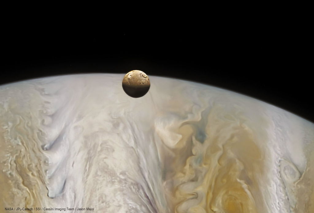 image of a brown small moon in front of a giant Jupiter