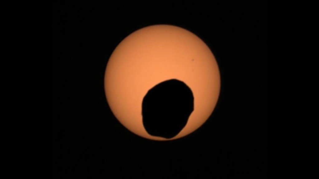 dark circle in front of orange sphere against a black background