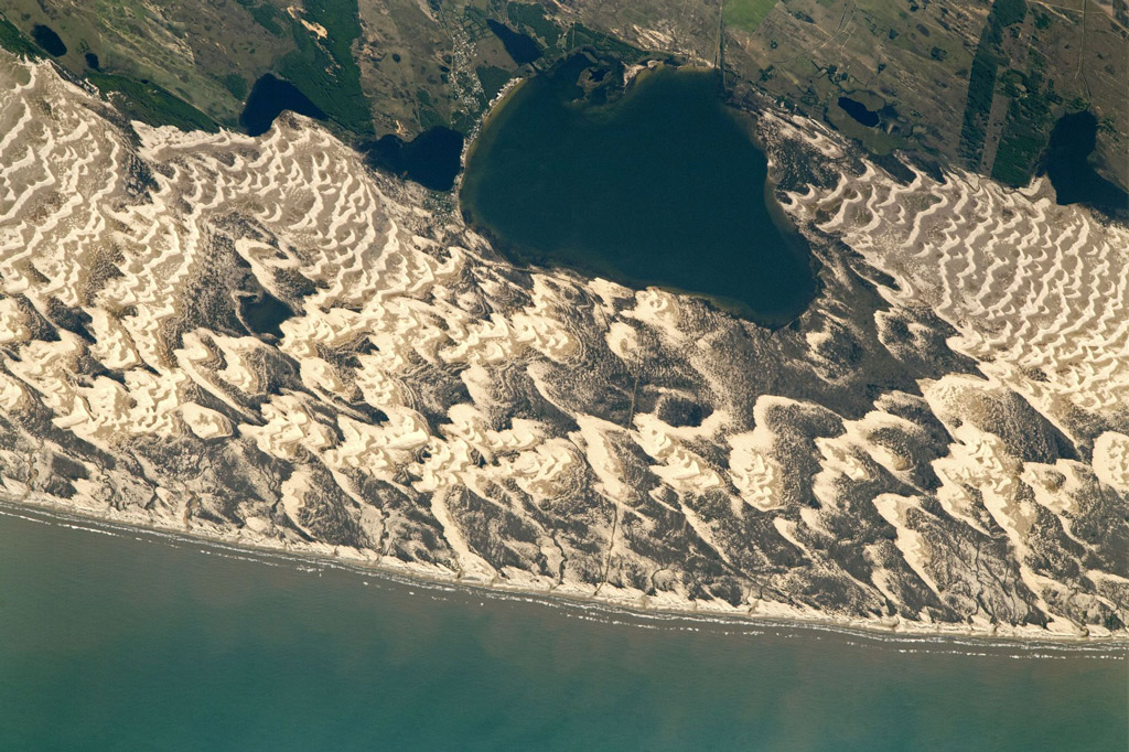 brown sand dunes on the coast creating beautiful ripples between an ocean and a mountainous lake
