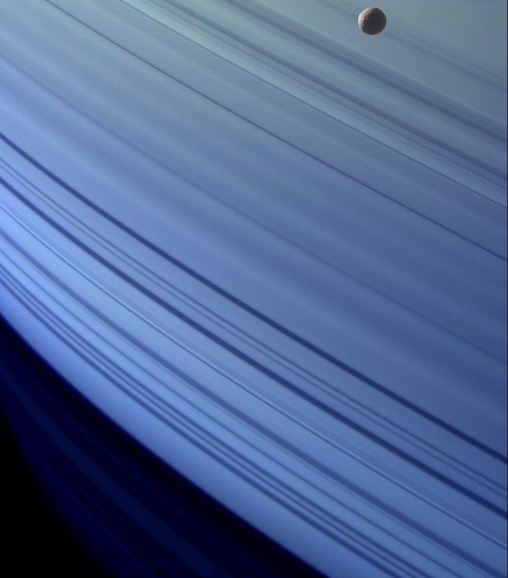 close up image of Saturn's rings with a small gray moon next to it.